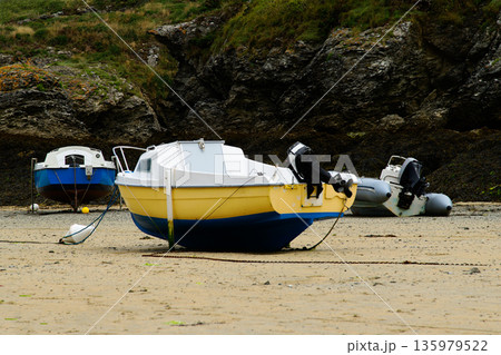 Colorful Small Boats Beached on Sandy Shore with Rocky Cliff Backdrop and Calm Tide 135979522