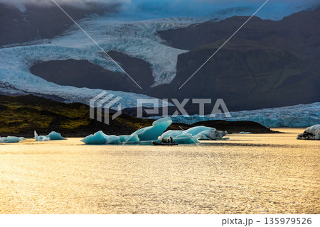 Fjallsarlon glacial lagoon showcases icebergs floating in calm waters, reflecting the soft twilight glow against the massive glacier backdrop. An iconic location in Iceland Fjallsarlon glacial lagoon showcases icebergs floating in calm waters, reflecting the soft twilight glow against the massive glacier backdrop. An iconic location in Iceland 135979526