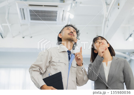 エアコンを見て不満そうな表情のビジネスウーマンと作業員 エアコンを見て不満そうな表情のビジネスウーマンと作業員 135980036