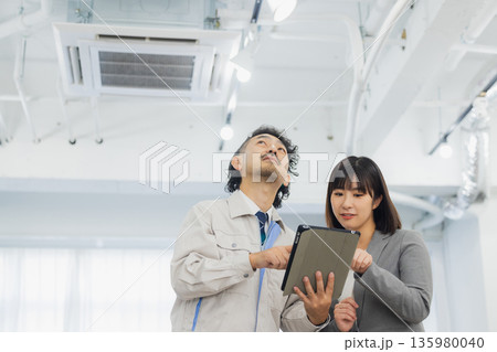 エアコンを見て不満そうな表情のビジネスウーマンと作業員 エアコンを見て不満そうな表情のビジネスウーマンと作業員 135980040