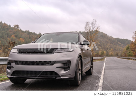 row of cars. Luxury SUV parked on the roadside under cloudy skies with green hills in the background during late autumn 135981022