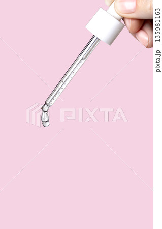 Pipette with serum in hand. Drips drop isolated on pink background, vertical photo copy space close up Pipette with serum in hand. Drips drop isolated on pink background, vertical photo copy space close up 135981163