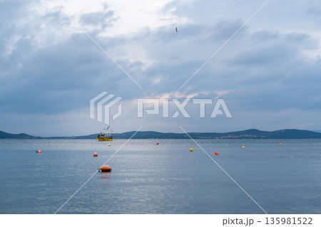 boats anchored in the sea. Fishing boat floats in calm water as clouds gather over the horizon during twilight hours boats anchored in the sea. Fishing boat floats in calm water as clouds gather over the horizon during twilight hours 135981522
