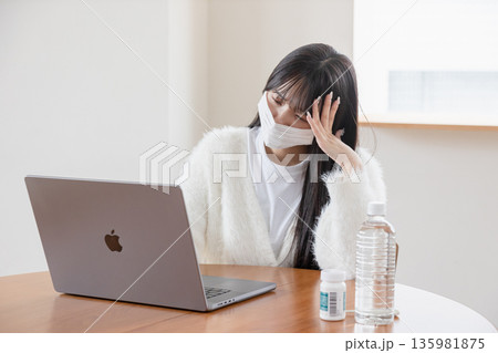 体調不良でも自宅でパソコンを操作する女性 体調不良でも自宅でパソコンを操作する女性 135981875