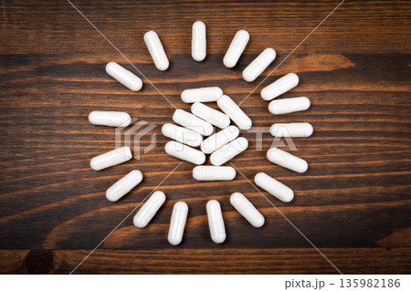 White Medical Capsules Arranged In Circular Pattern On Wooden Background White Medical Capsules Arranged In Circular Pattern On Wooden Background 135982186