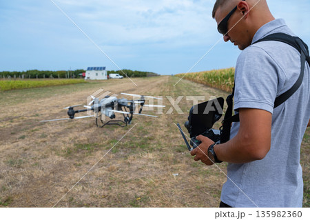 Drone operator outdoors with field drone on farm using remote controller for farming technology 135982360