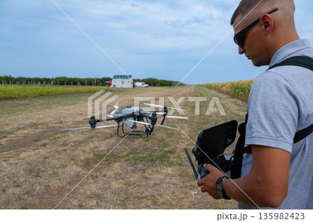Drone pilot operating handheld controller in open field with quadcopter ready to fly 135982423
