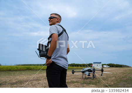 Drone pilot with controller stands in field preparing quadcopter for takeoff outdoors 135982434