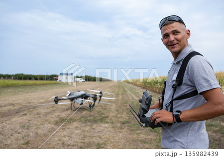 Drone pilot in a field with controller beside a drone, preparing agricultural surveillance 135982439