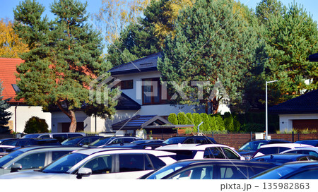 Cars parked at large parking lot. The back is a single family house covered with trees. Cars parked at large parking lot. The back is a single family house covered with trees. 135982863