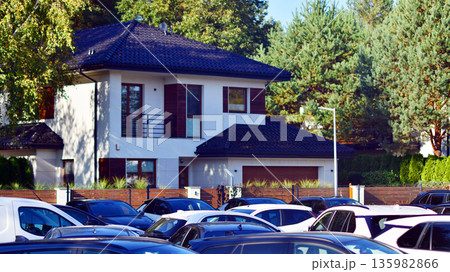 Cars parked at large parking lot. The back is a single family house covered with trees. Cars parked at large parking lot. The back is a single family house covered with trees. 135982866