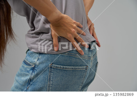 Close-up of person holding lower back in pain, showing discomfort Close-up of person holding lower back in pain, showing discomfort 135982869