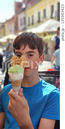 Portrait of a smiling teenage boy holding a colorful ice cream cone with a heart-shaped cookie Portrait of a smiling teenage boy holding a colorful ice cream cone with a heart-shaped cookie 135983423