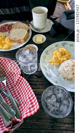 Outdoor breakfast spread with eggs, salami, bread, and coffee on a wooden table Outdoor breakfast spread with eggs, salami, bread, and coffee on a wooden table 135985487