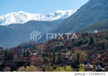 Mountains of Atlas loom over village in Morocco with rich greenery and snow-capped peaks 135986255
