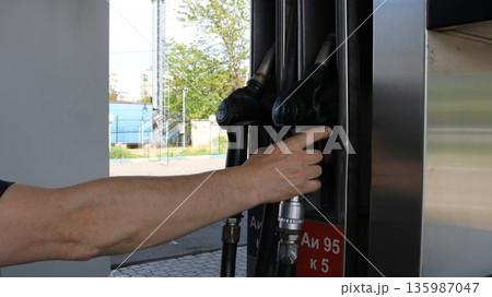 A white man's hand picks up or places a pistol at a gas station with Russian markings for AI-95 gasoline. A driver refueling with expensive, high-quality gasoline in Russia. A white man's hand picks up or places a pistol at a gas station with Russian markings for AI-95 gasoline. A driver refueling with expensive, high-quality gasoline in Russia. 135987047