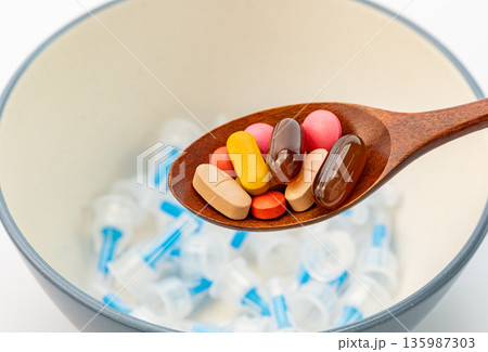 Medical choice between pills and injection, wooden spoon with supplements and syringe needles for healthcare treatment concept 135987303