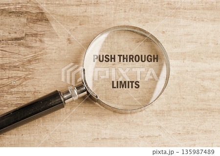 A magnifying glass rests on a light brown wooden surface, clearly enlarging the empowering words PUSH THROUGH LIMITS A magnifying glass rests on a light brown wooden surface, clearly enlarging the empowering words PUSH THROUGH LIMITS 135987489