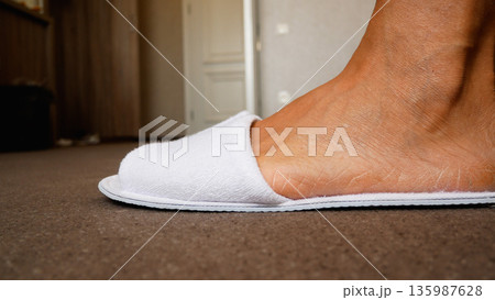 Close-up. The women's feet in the room put on white hotel slippers Close-up. The women's feet in the room put on white hotel slippers 135987628