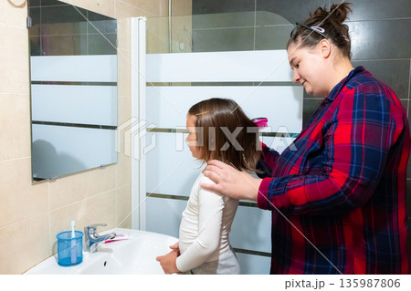 Caucasian adult female brushing young female child hair in bathroom 135987806