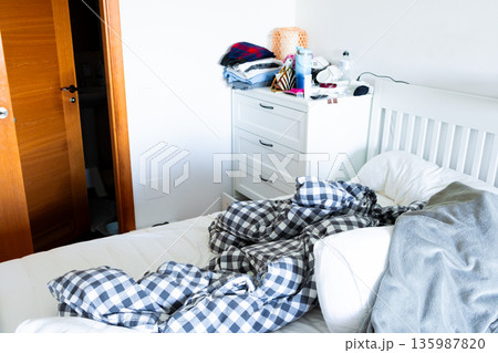 Cozy bedroom scene with unmade bed and wooden door 135987820