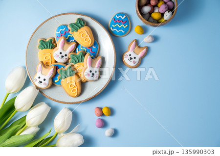 Easter spring holiday background with easter cookies in a plate: bunny, carrot and egg with white tulips Easter spring holiday background with easter cookies in a plate: bunny, carrot and egg with white tulips 135990303