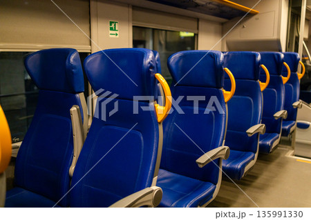 interior of a modern train or bus with rows of blue seats, and a central aisle, all unoccupied, public transportation 135991330