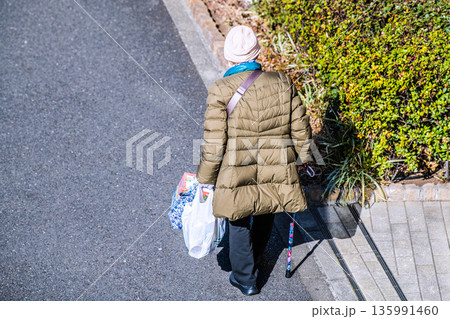 日本の横浜都市景観光と“陰”…高齢化社会　杖の高齢女性（マスク姿）。買い物帰り、左手は手袋… 135991460