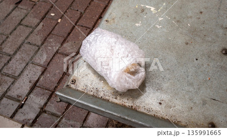 Parcel wrapped in bubble wrap on dirty metal surface next to brick pavement. Unknown object and concept of hidden danger. Parcel wrapped in bubble wrap on dirty metal surface next to brick pavement. Unknown object and concept of hidden danger. 135991665