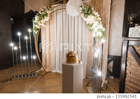 Elegant Wedding Arch with White Flowers and Gold Accents Surrounded by Candlelight in a Romantic Indoor Setting Elegant Wedding Arch with White Flowers and Gold Accents Surrounded by Candlelight in a Romantic Indoor Setting 135992343