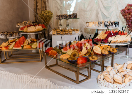 Elegant Fruit and Dessert Buffet Display with Assorted Sliced Fruits, Pastries, and Decorative Glass Stands in Luxury Event Setting Elegant Fruit and Dessert Buffet Display with Assorted Sliced Fruits, Pastries, and Decorative Glass Stands in Luxury Event Setting 135992347
