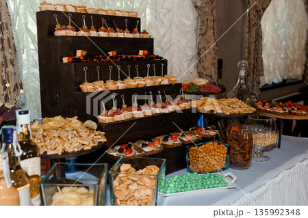 Elegant tiered snack station with appetizers, chips, and candies at a festive party or wedding reception Elegant tiered snack station with appetizers, chips, and candies at a festive party or wedding reception 135992348