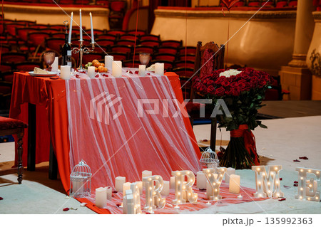 Romantic Proposal Setup in Grand Theater with Red Roses, Candlelit Table, and "MARRY ME" Lights 135992363
