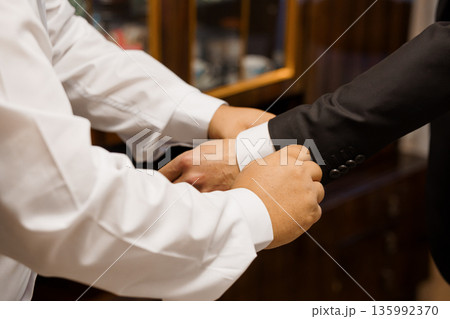 Tailor Adjusting Black Suit Jacket Sleeve on White Shirt in Elegant Wood-Framed Dressing Room Setting Tailor Adjusting Black Suit Jacket Sleeve on White Shirt in Elegant Wood-Framed Dressing Room Setting 135992370