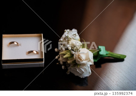 Elegant Wedding Rings and White Rose Boutonniere in Gold Box on Dark Surface Elegant Wedding Rings and White Rose Boutonniere in Gold Box on Dark Surface 135992374