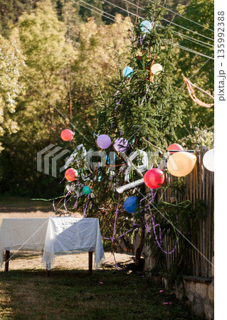 Colorful Balloon Decorated Christmas Tree Outdoors in Forest Setting with White Tablecloth and Natural Light Colorful Balloon Decorated Christmas Tree Outdoors in Forest Setting with White Tablecloth and Natural Light 135992388