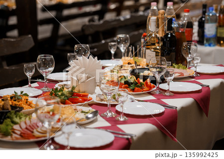 Elegant Banquet Table Setup with Assorted Delicacies, Wine Bottles, and Fine Glassware on Red and White Checkered Tablecloth 135992425