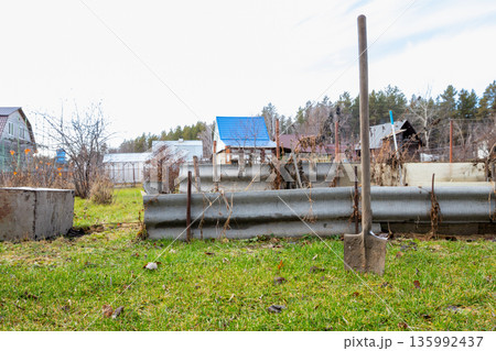 Shovel standing in green grass in the village, signifying garden work, rural life, and the start of the gardening season. Shovel standing in green grass in the village, signifying garden work, rural life, and the start of the gardening season. 135992437