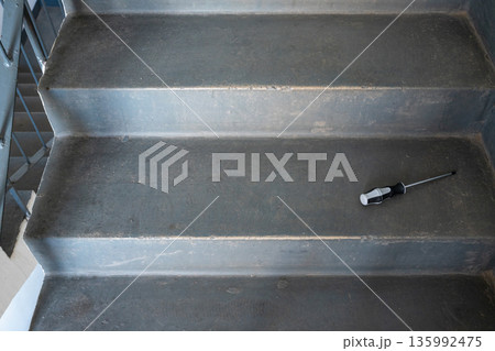 Screwdriver on gray concrete staircase. Maintenance and repair concept for construction, building, or renovation projects. Tool for home improvement. 135992475