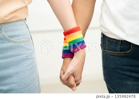 Asian LGBT couple woman holding hand wearing rainbow wristband. 135992478