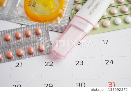 Pregnancy test with birth control pills and condom for female on calendar, ovulation day. Pregnancy test with birth control pills and condom for female on calendar, ovulation day. 135992872