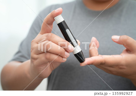 Asian woman self testing to check blood sugar level diabetes by digital lancet on finger at home. 135992927