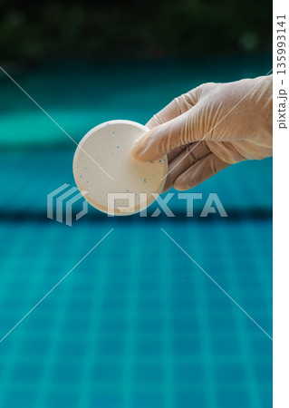 Gloved hand holding chlorine tablet above blue swimming pool water, outdoor pool maintenance and water sanitation concept with clear background Gloved hand holding chlorine tablet above blue swimming pool water, outdoor pool maintenance and water sanitation concept with clear background 135993141