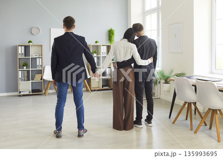 Office love triangle as woman hugs one colleague and secretly holds another's hand 135993695