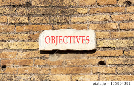 Objectives symbol. Concept word Objectives on beautiful white marble sign plate. Beautiful ancient brick wall background. Business objectives concept. Copy space. 135994391