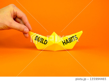 Build habits symbol. Concept word Build habits on beautiful yellow paper boat. Businessman's hand. Beautiful orange paper background. Business build habits concept. Copy space. Build habits symbol. Concept word Build habits on beautiful yellow paper boat. Businessman's hand. Beautiful orange paper background. Business build habits concept. Copy space. 135994465