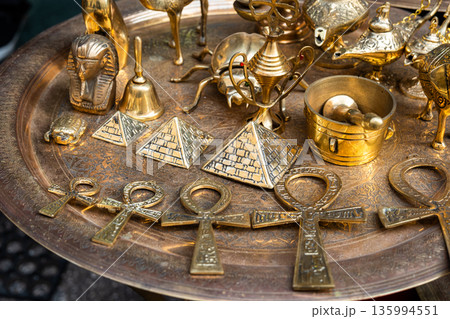 Golden figures and artefacts are displayed on a tray in Khan El Khalili market in Cairo, Egypt. Items include ankh symbols, pyramids, and decorative bowls Golden figures and artefacts are displayed on a tray in Khan El Khalili market in Cairo, Egypt. Items include ankh symbols, pyramids, and decorative bowls 135994551