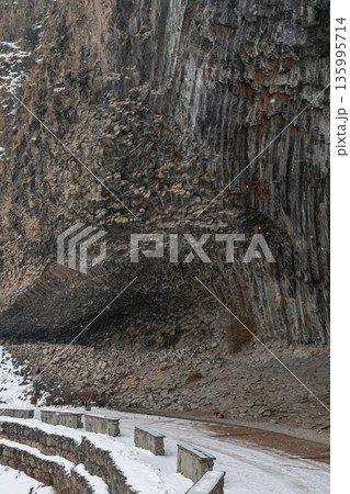 Snow-covered road curves along massive basalt cliffs at Symphony of Stones, layered volcanic rock and stone barriers shape dramatic winter landscape. Snow-covered road curves along massive basalt cliffs at Symphony of Stones, layered volcanic rock and stone barriers shape dramatic winter landscape. 135995714