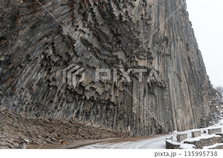 Towering vertical basalt columns form monumental cliff at Symphony of Stones, dramatic volcanic geometry rises above a winter road Towering vertical basalt columns form monumental cliff at Symphony of Stones, dramatic volcanic geometry rises above a winter road 135995738