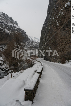 Snow-covered road and river run alongside towering basalt columns at the Symphony of Stones, dark volcanic textures contrast with winter whites Snow-covered road and river run alongside towering basalt columns at the Symphony of Stones, dark volcanic textures contrast with winter whites 135995743
